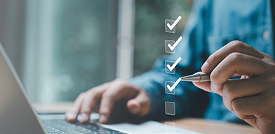 person checking items on a digital checklist while using a laptop for task management and organization